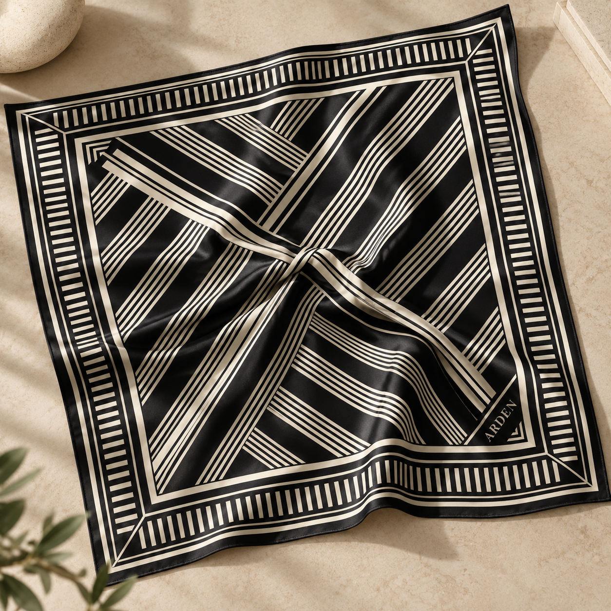 ARDEN black and cream striped corporate bandana laid flat on beige stone, showing the diagonal stripes, striped border, and ARDEN corner mark